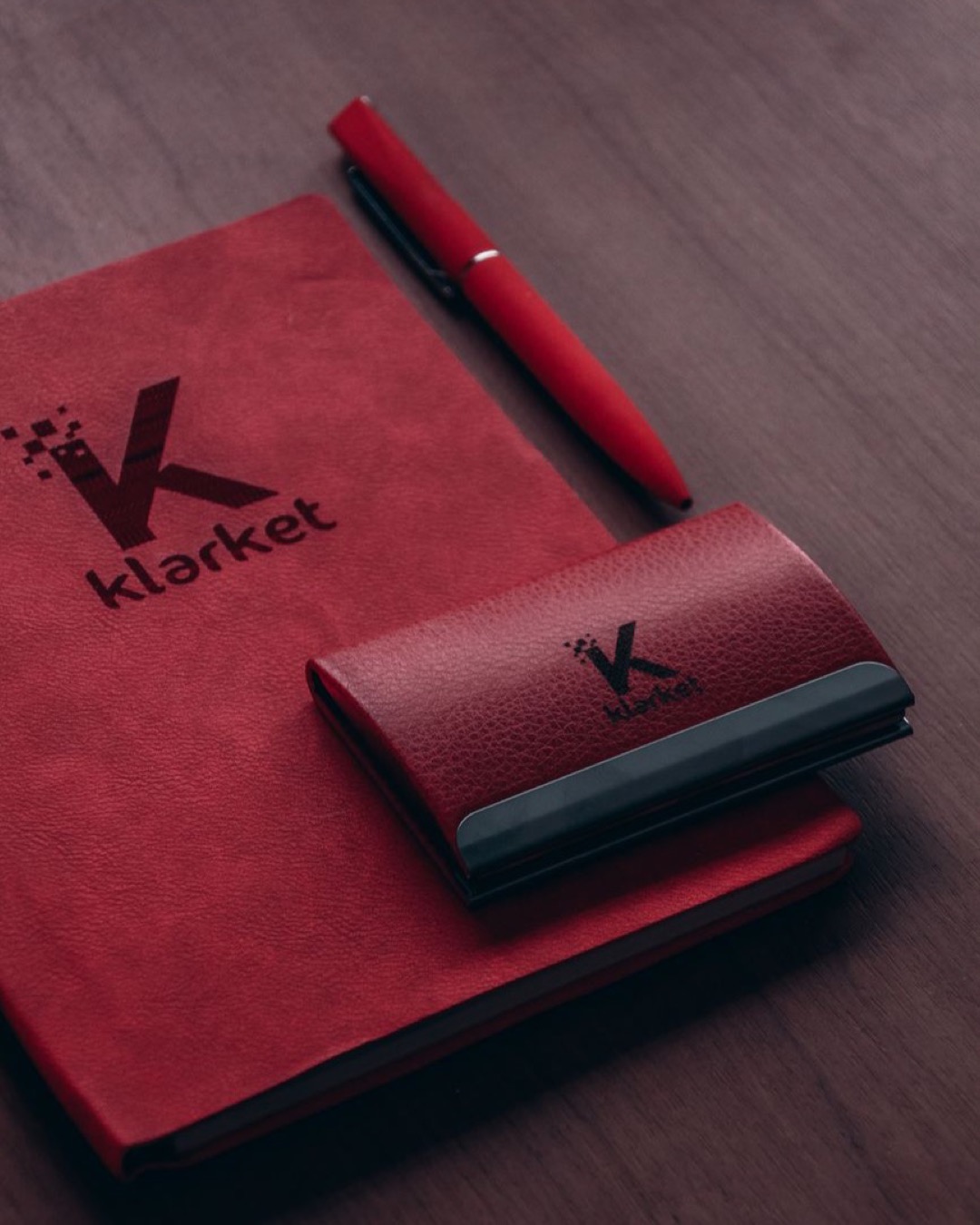 Red notebook with branding and pen on wooden desk, ideal for office themes.