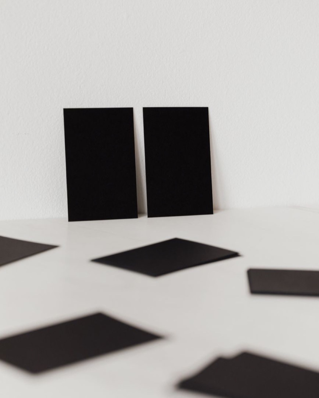 Collection of black mockup business cards placed against white wall and scattered on white surface