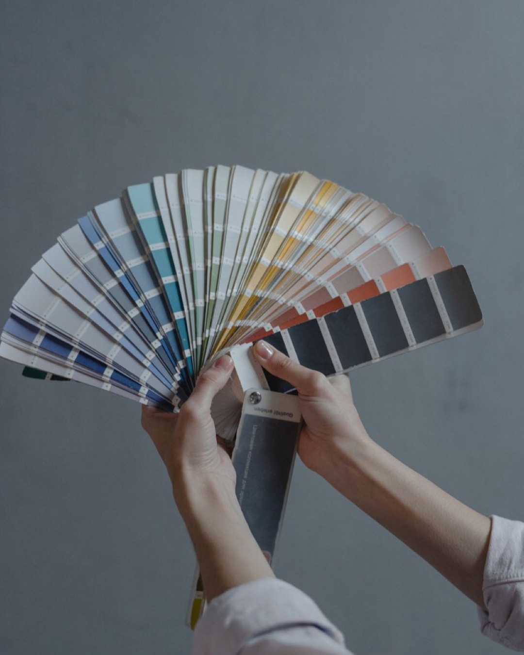 Hands holding color swatch samples in a fan shape against a gray background.