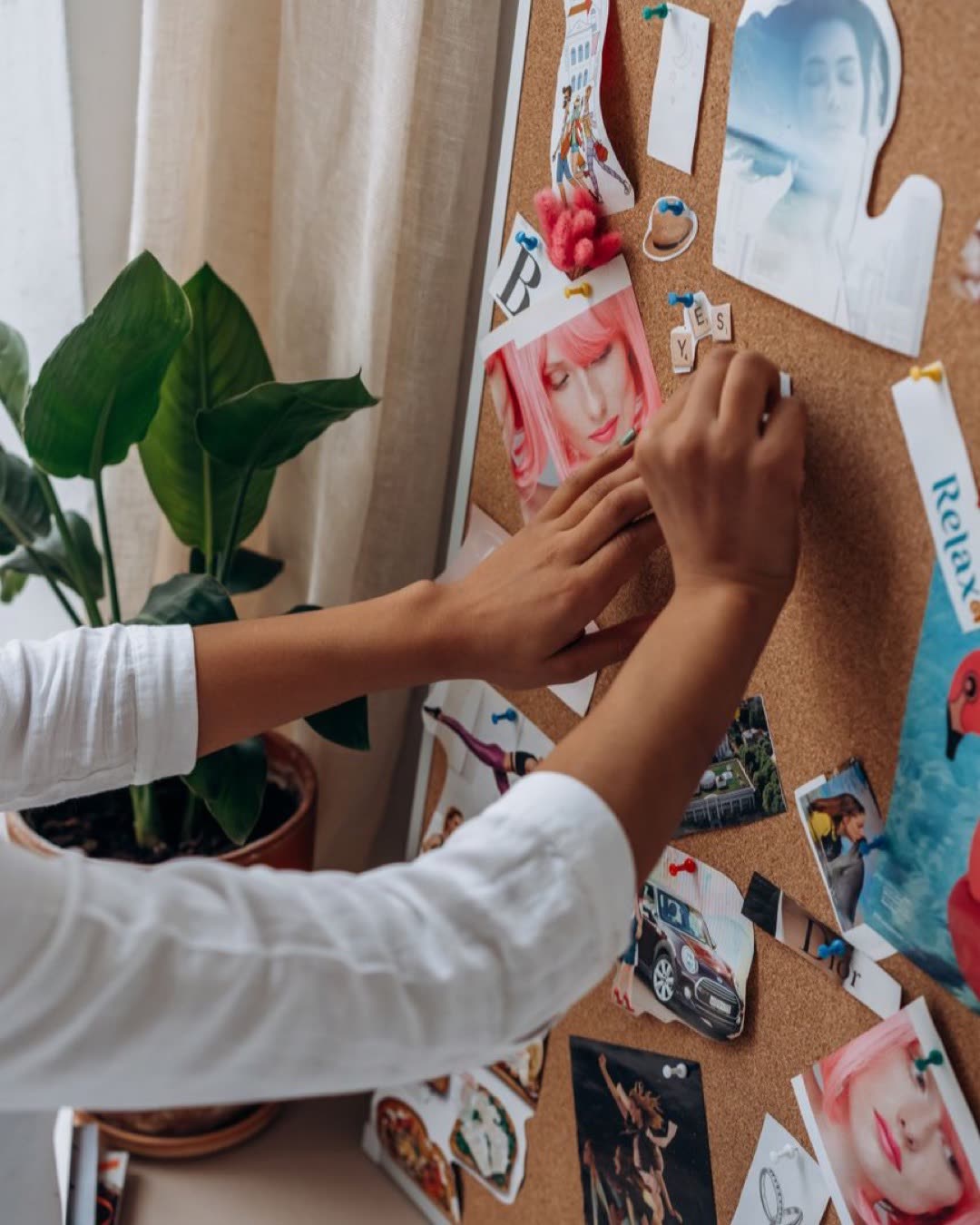 A person arranging photos and notes on a cork board, adding a personal touch to a creative workspace.
