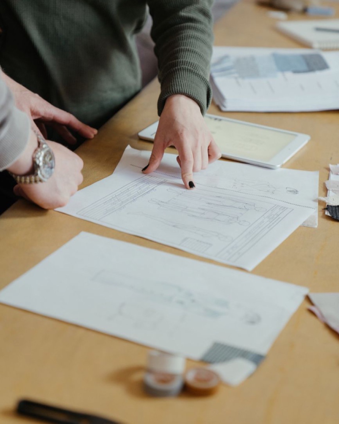 Two fashion designers review clothing sketches in a creative workspace, focusing on design plans.