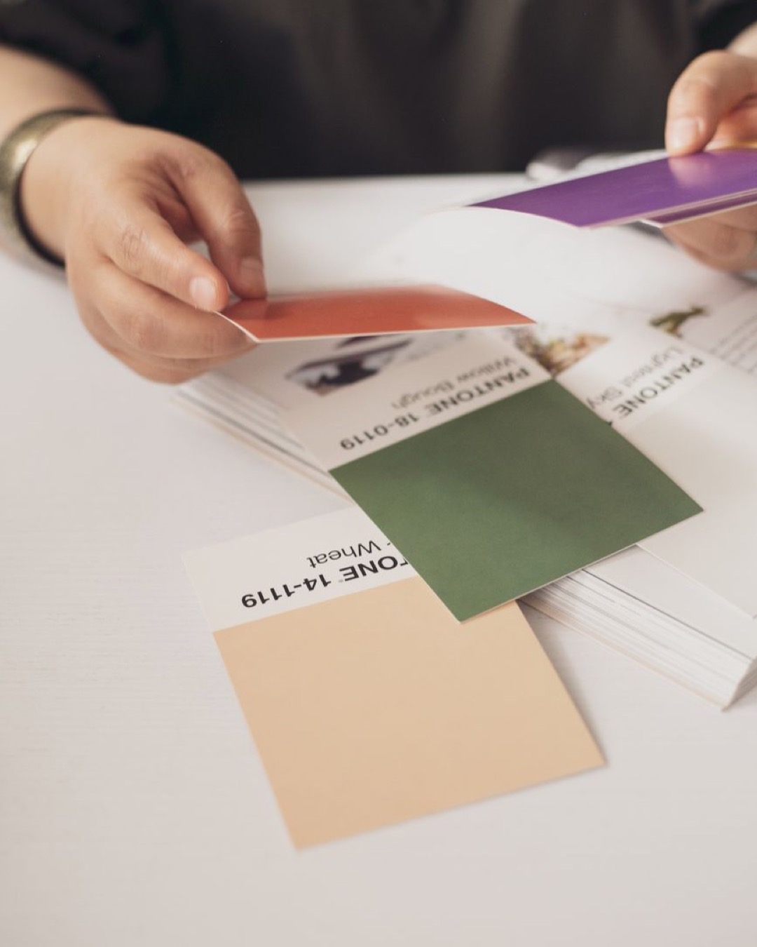 Close-up of hands selecting Pantone color swatches in a creative setting.