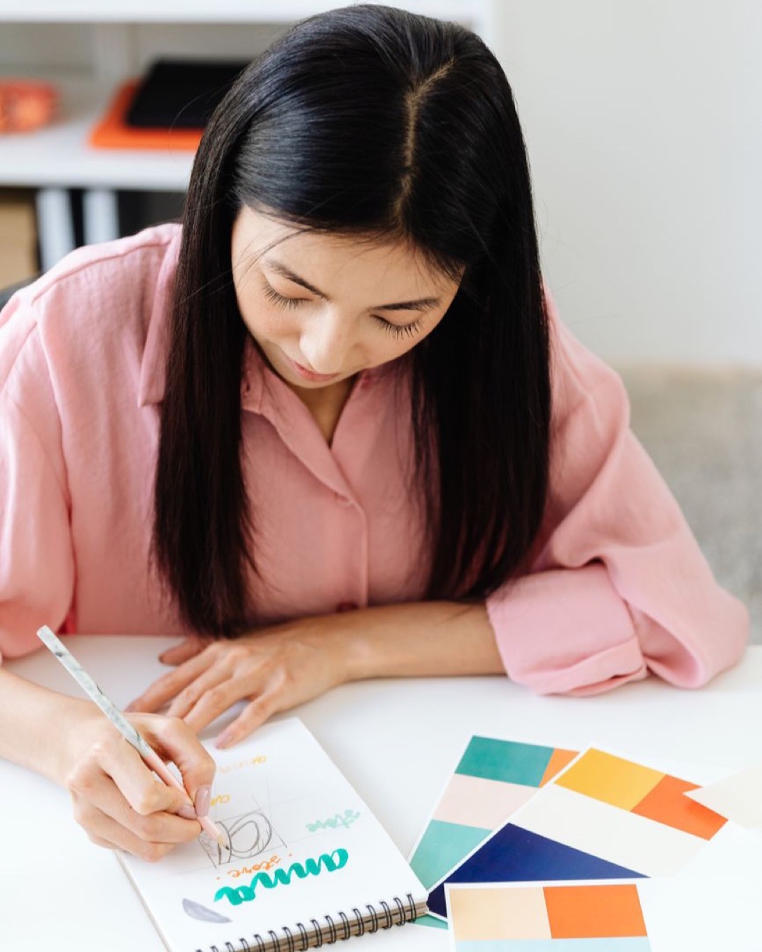 Woman designing with color swatches and sketchpad in office.