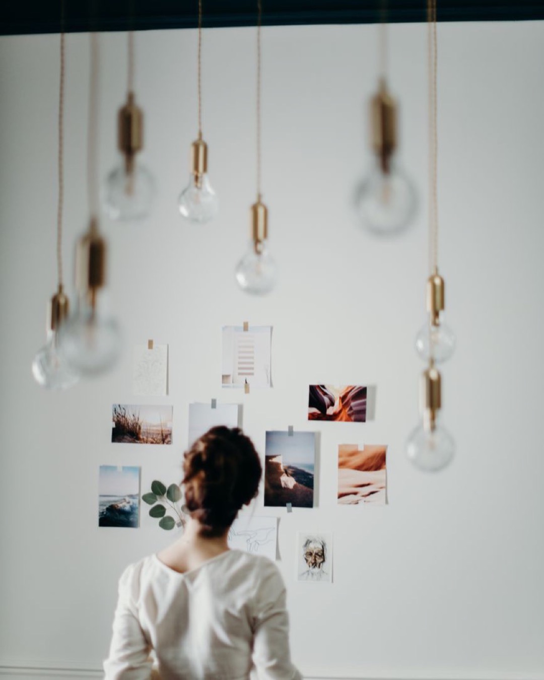 Woman in white top examining mood board under hanging lights in a modern interior design setting.
