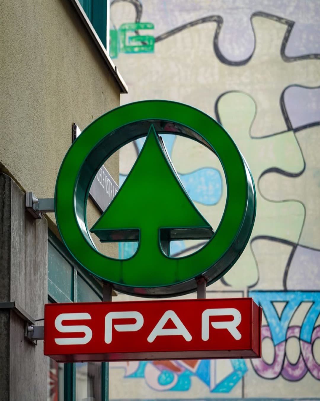 Vibrant SPAR supermarket sign against a colorful urban mural backdrop.
