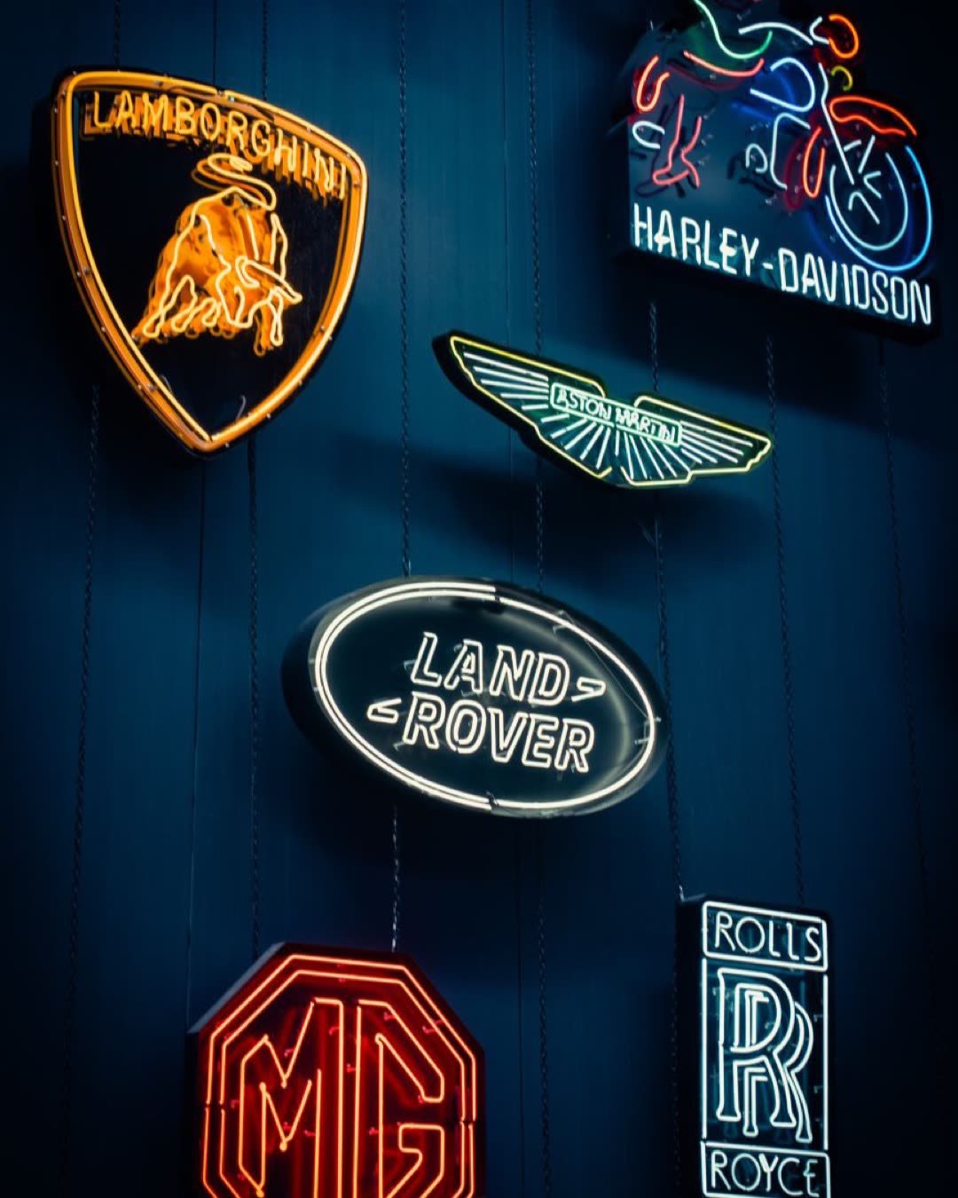Vibrant neon signs showcasing luxury vehicle brands and logos in a dark, moody setting.