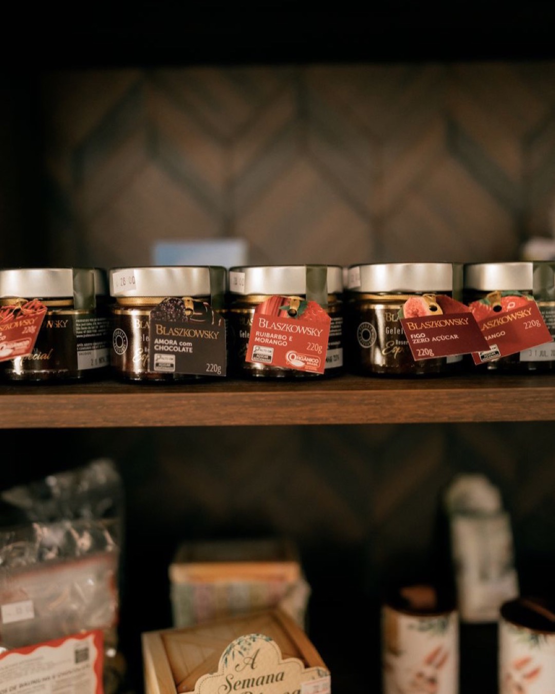 Assorted jars of jam displayed on a wooden shelf in a rustic setting.