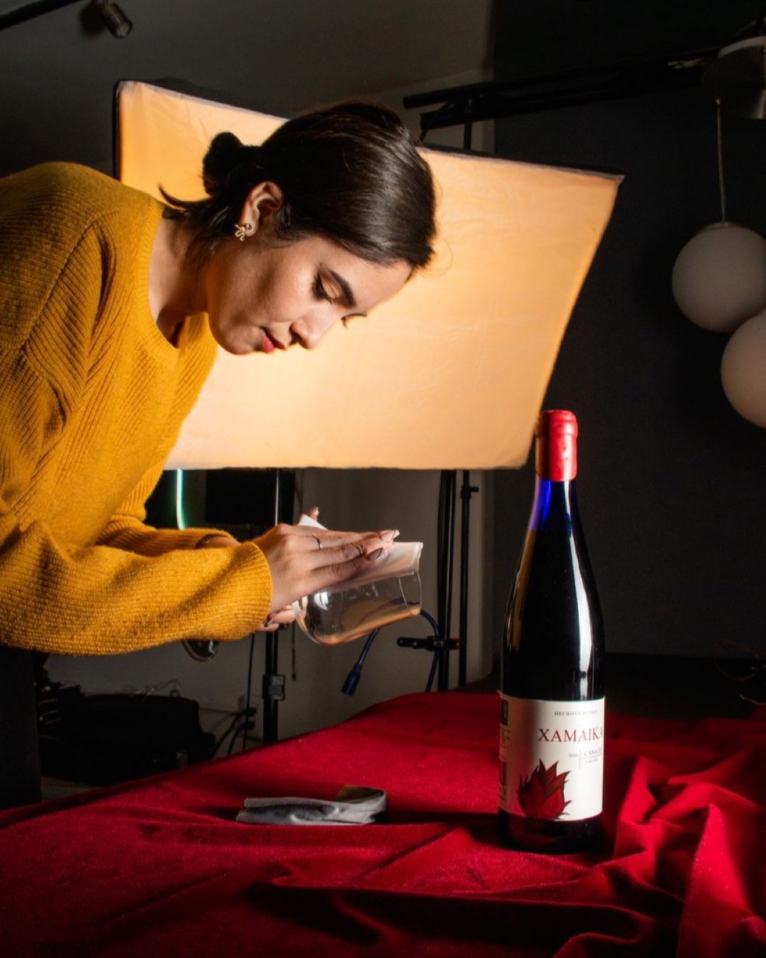 A woman arranges a photoshoot setup with wine bottle and lighting in a studio.