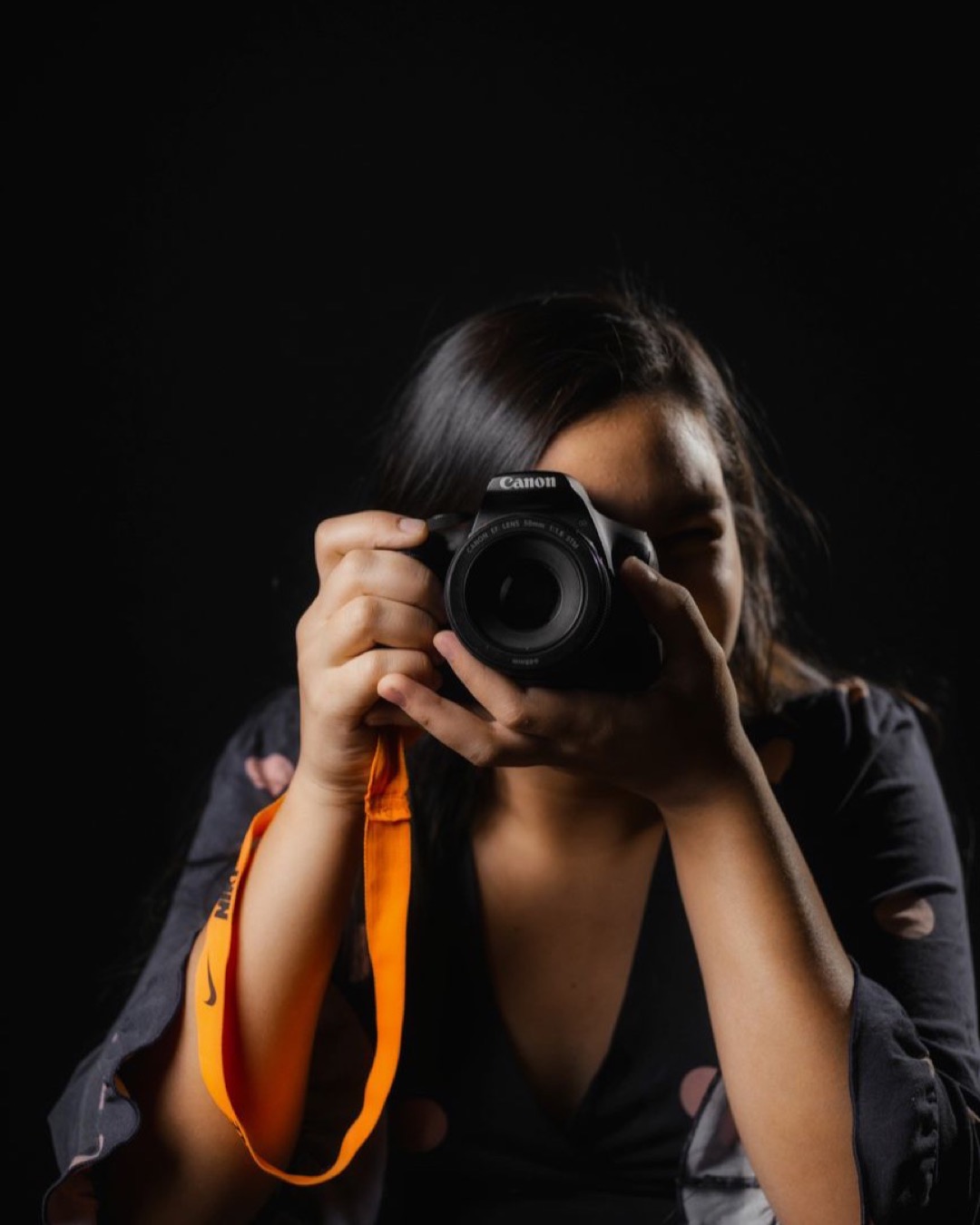 Studio shot of a woman photographer taking a picture with a camera against a black backdrop.