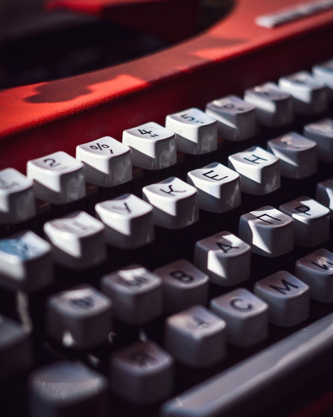 Detailed close-up of a red vintage typewriter, highlighting sunlit keys with Cyrillic letters.