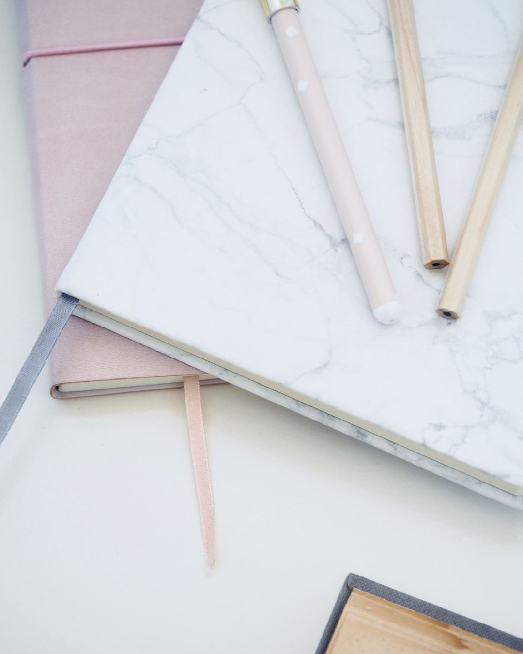 Stylish marble and pink notebooks paired with pens, creating an elegant and clean office desk setup.