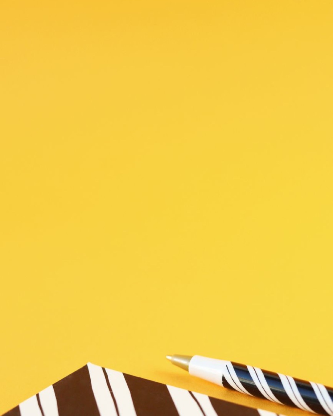 Minimalist composition with notebook and pen on vibrant yellow background, ideal for creative projects.