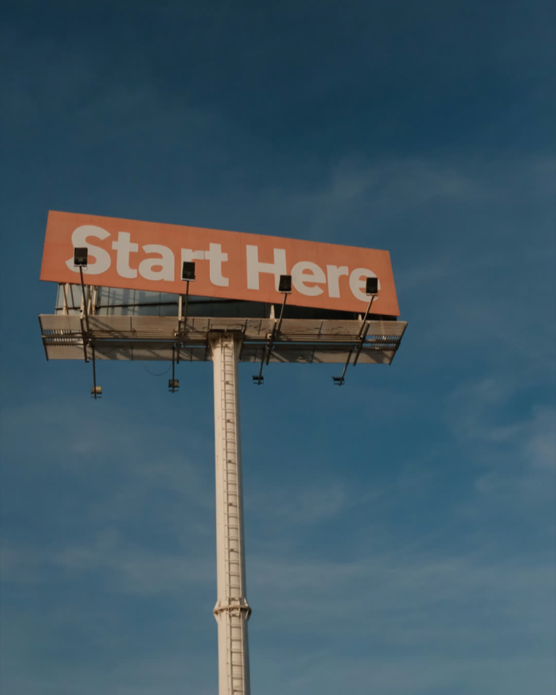 A tall billboard with 'Start Here' message set against a clear blue sky.