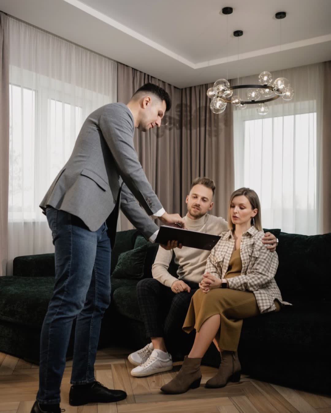 A real estate agent shows a document to an attentive couple seated on a sofa, indoors.