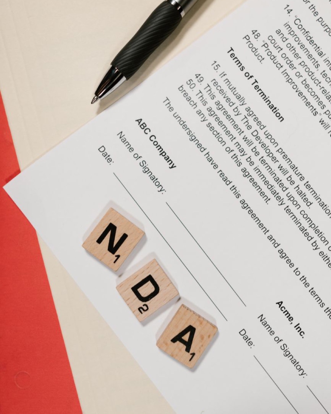 NDA document on table with Scrabble tiles and pen in office setting.