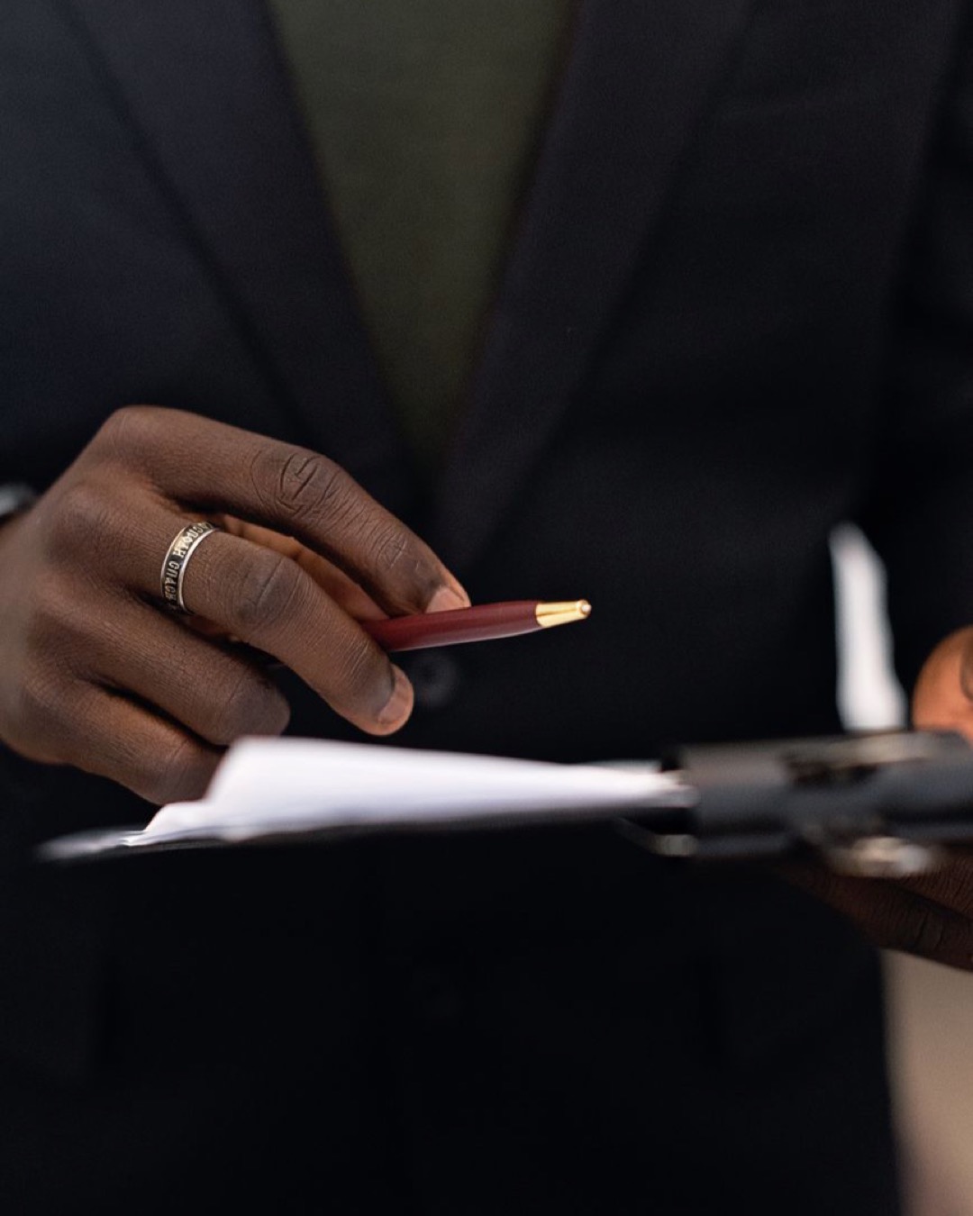 Close-up of a business professional holding a pen and reviewing documents on a clipboard.