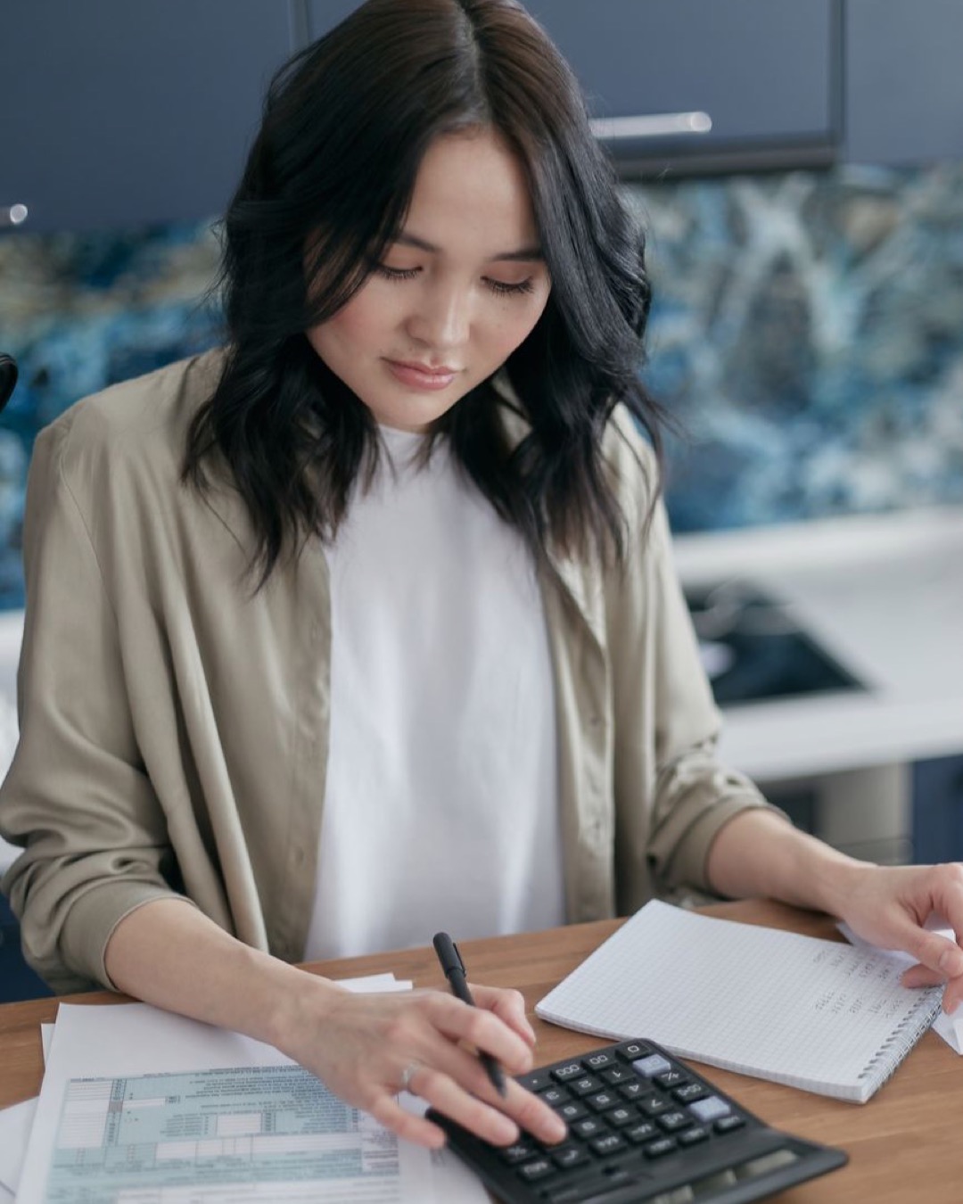Woman using a calculator for budgeting and finance management at home desk.