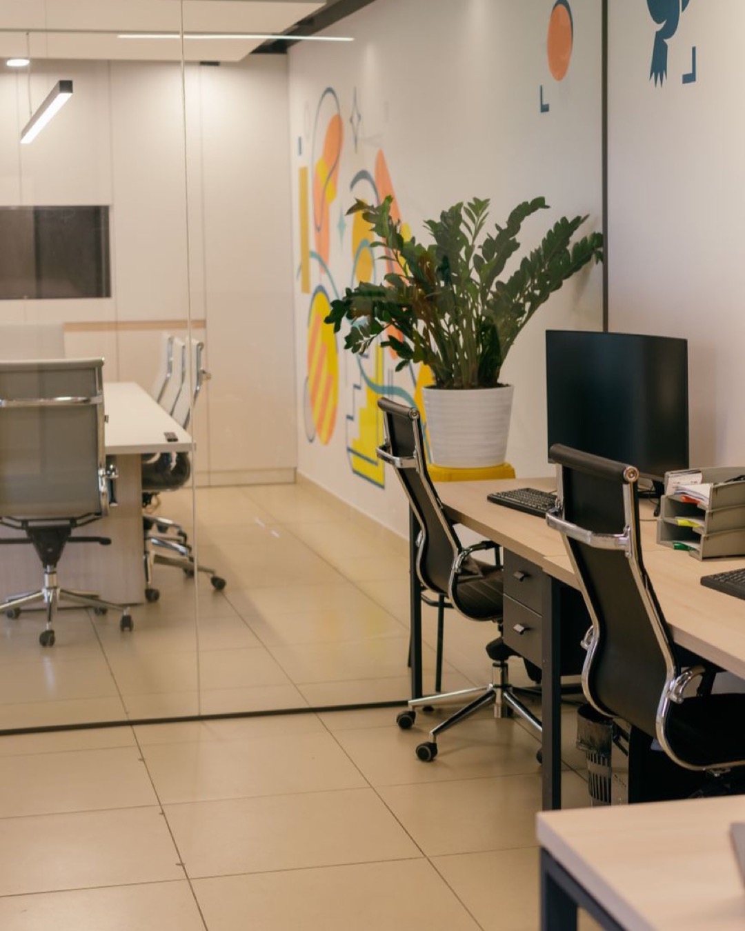 Spacious and contemporary office interior with glass partitions, stylish furniture, and vibrant wall art.