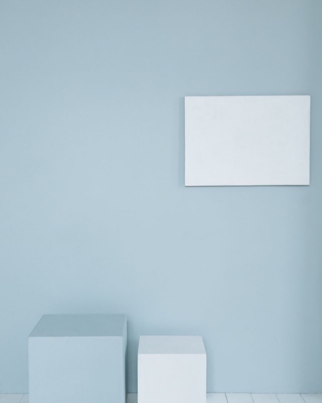 A minimalist room with a blank canvas on a pastel wall and two cubes for mockup design.