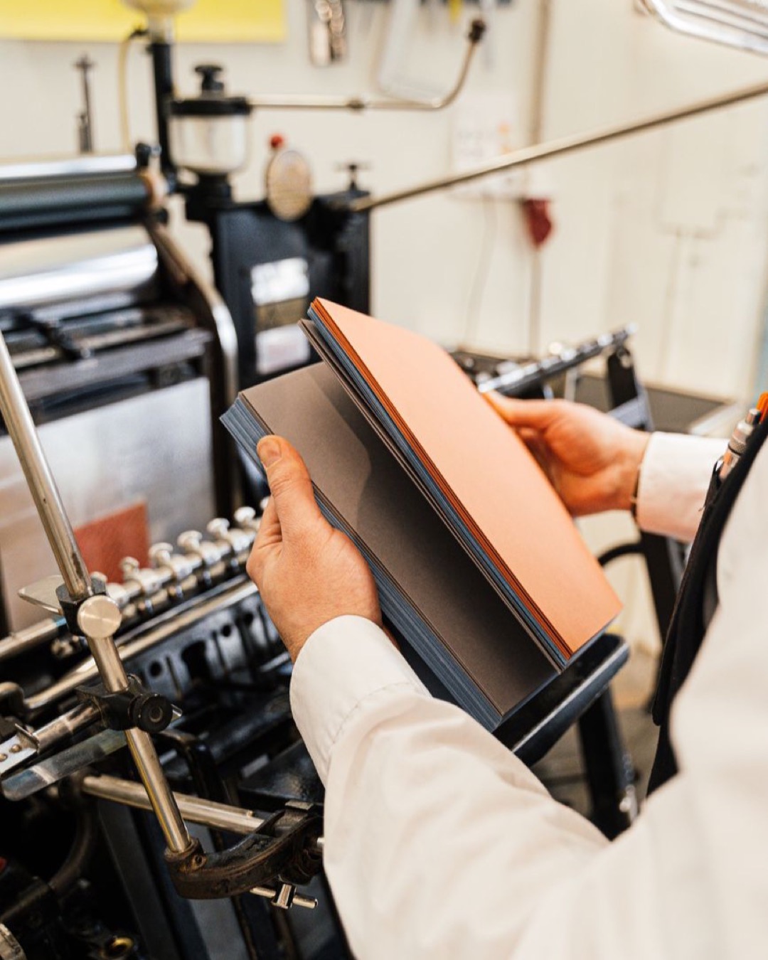 Person holding papers near a printing press in a workshop setting.