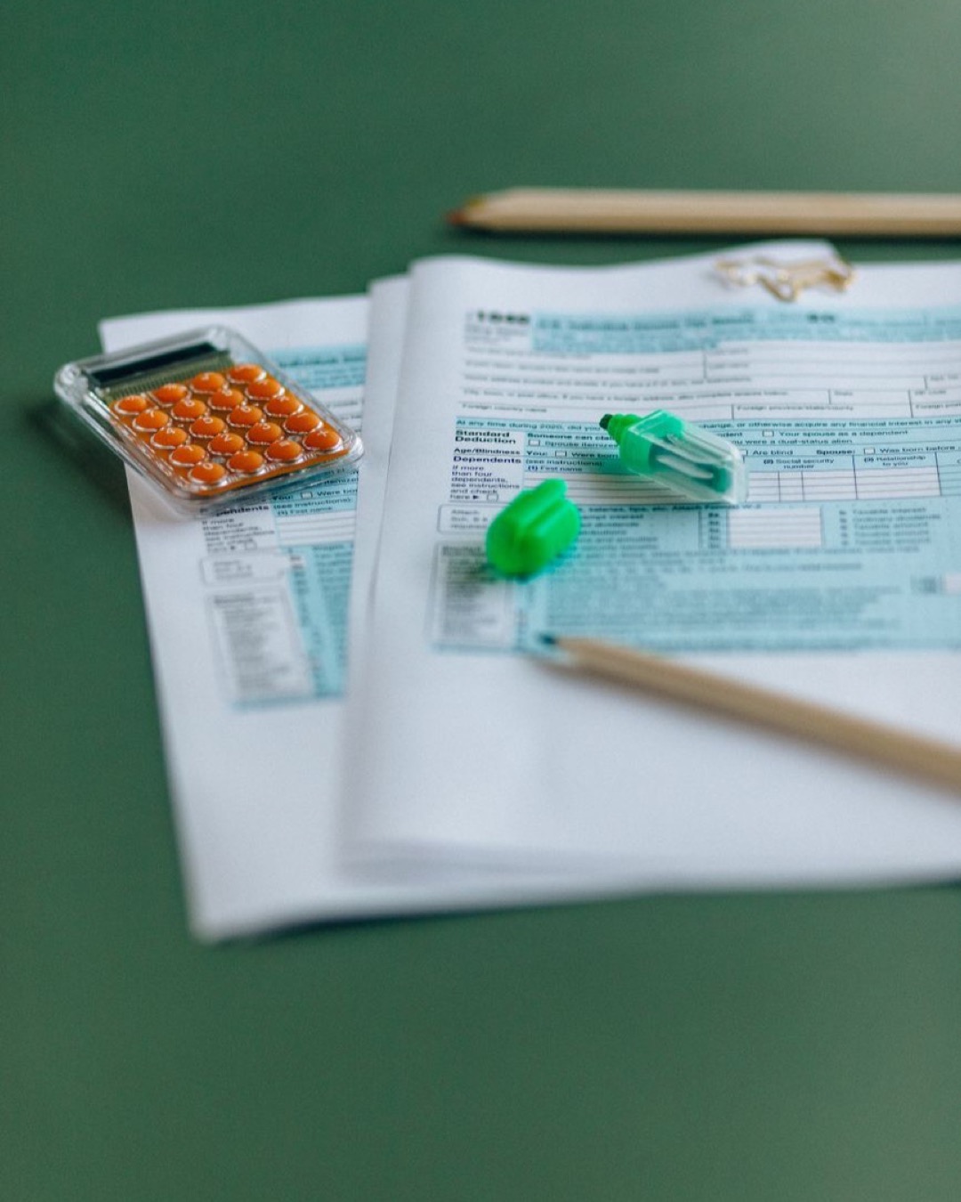 Close-up of tax documents with calculator on a green table, ideal for finance themes.