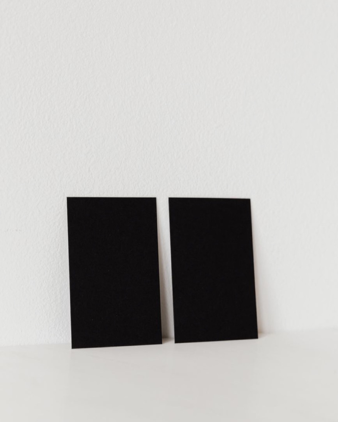 Pair of black business cards with no text leaning on white wall in studio