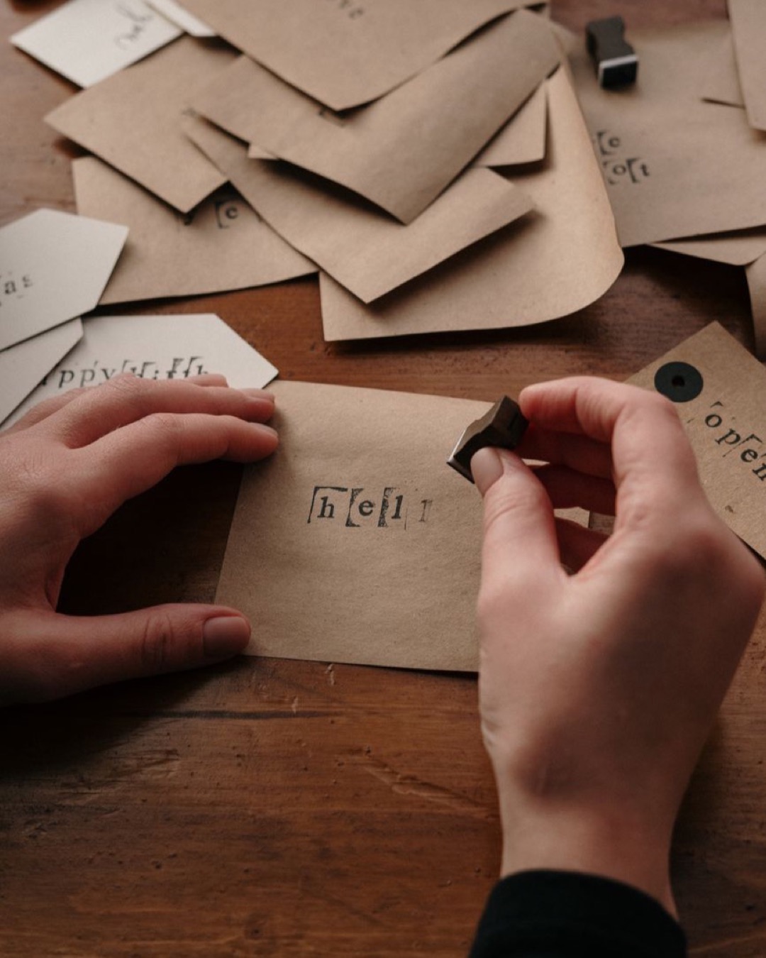 Hands stamping custom cards with love on a wooden desk.