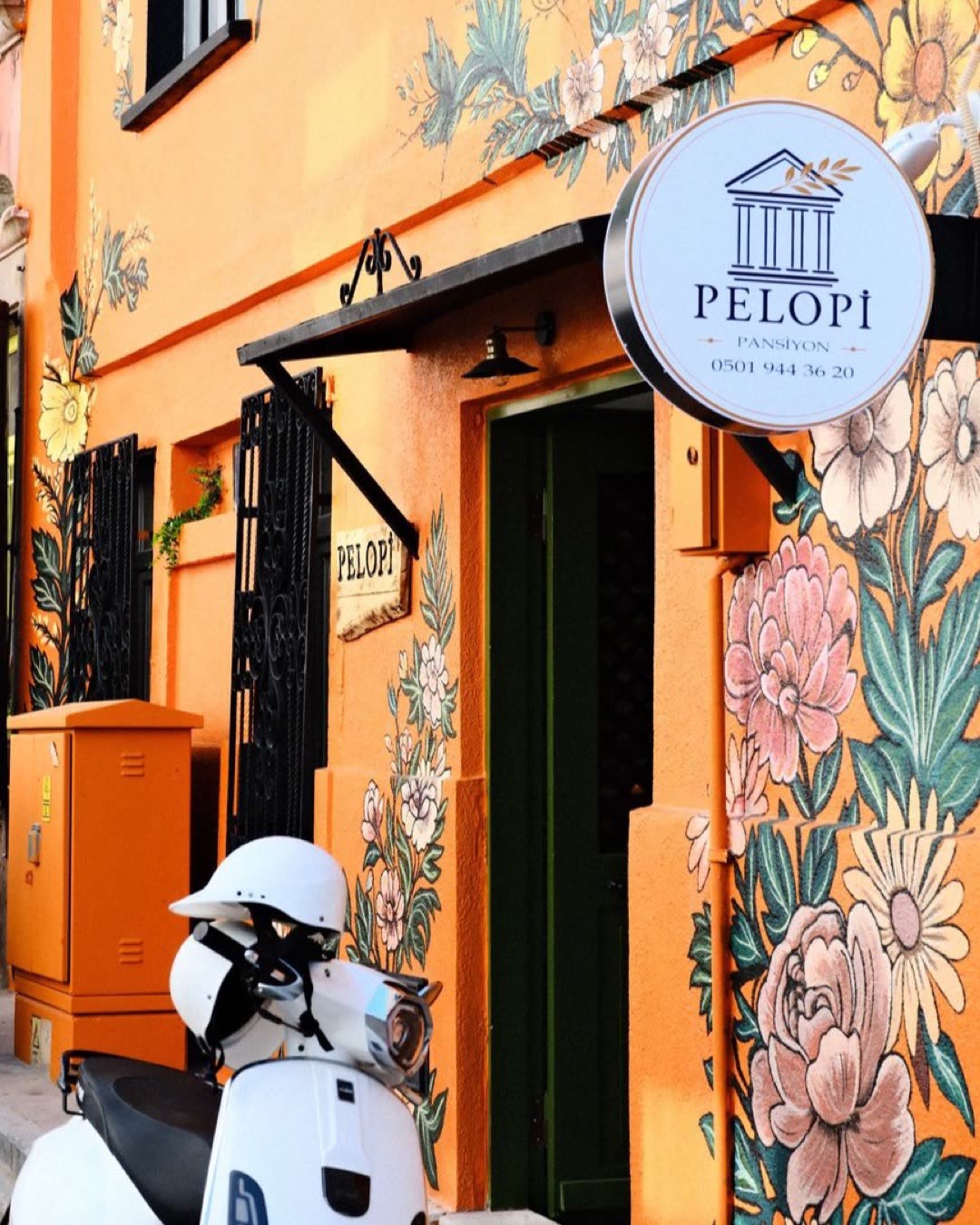 Colorful street art on building exterior featuring a vibrant floral mural with a Vespa parked outside.
