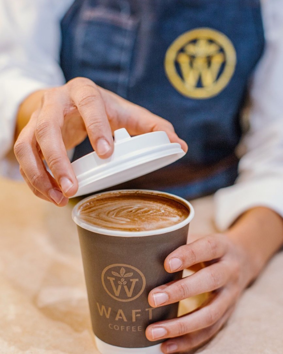 Close-up of latte in paper cup held by a barista in Baku, Azerbaijan.