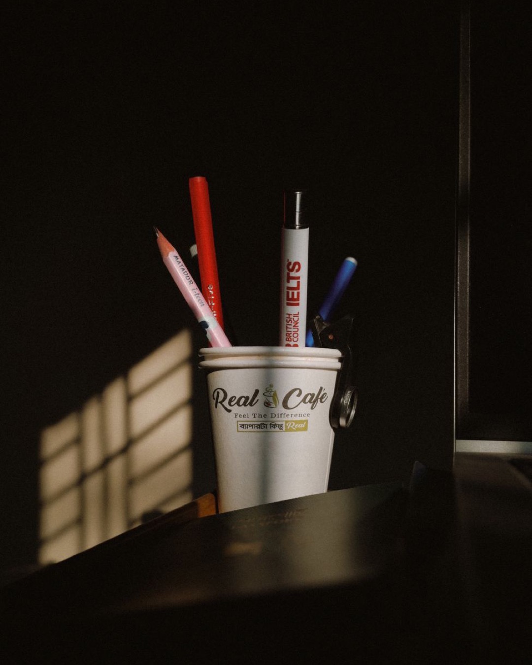 A creative desk arrangement with a cup holding pens and pencils illuminated by warm sunlight, casting intriguing shadows