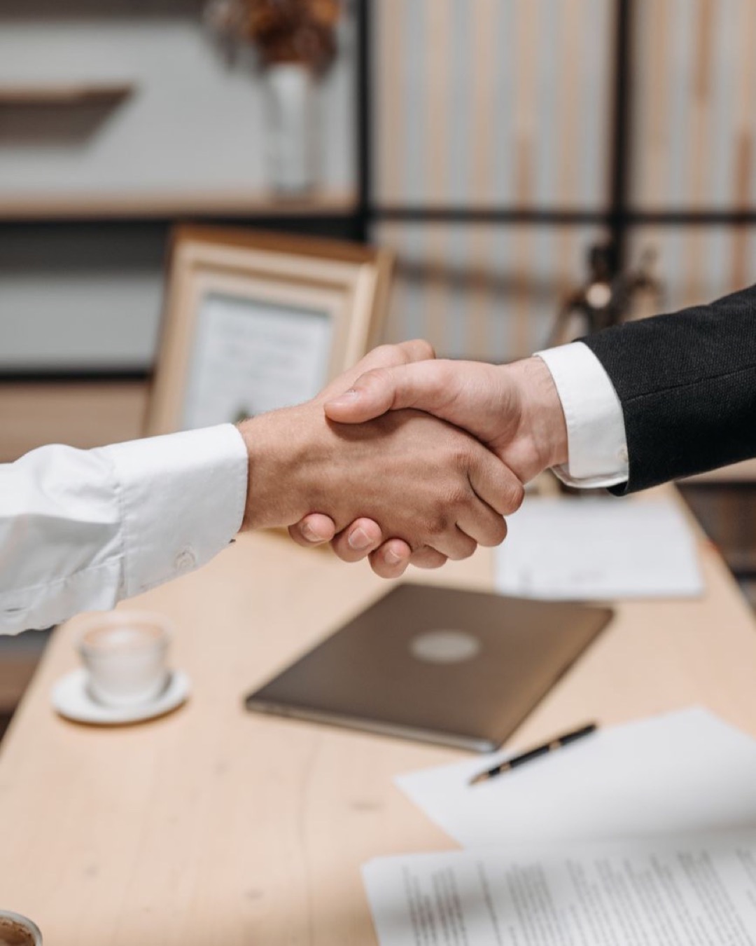 Close-up of two people shaking hands in an office, symbolizing agreement and partnership.