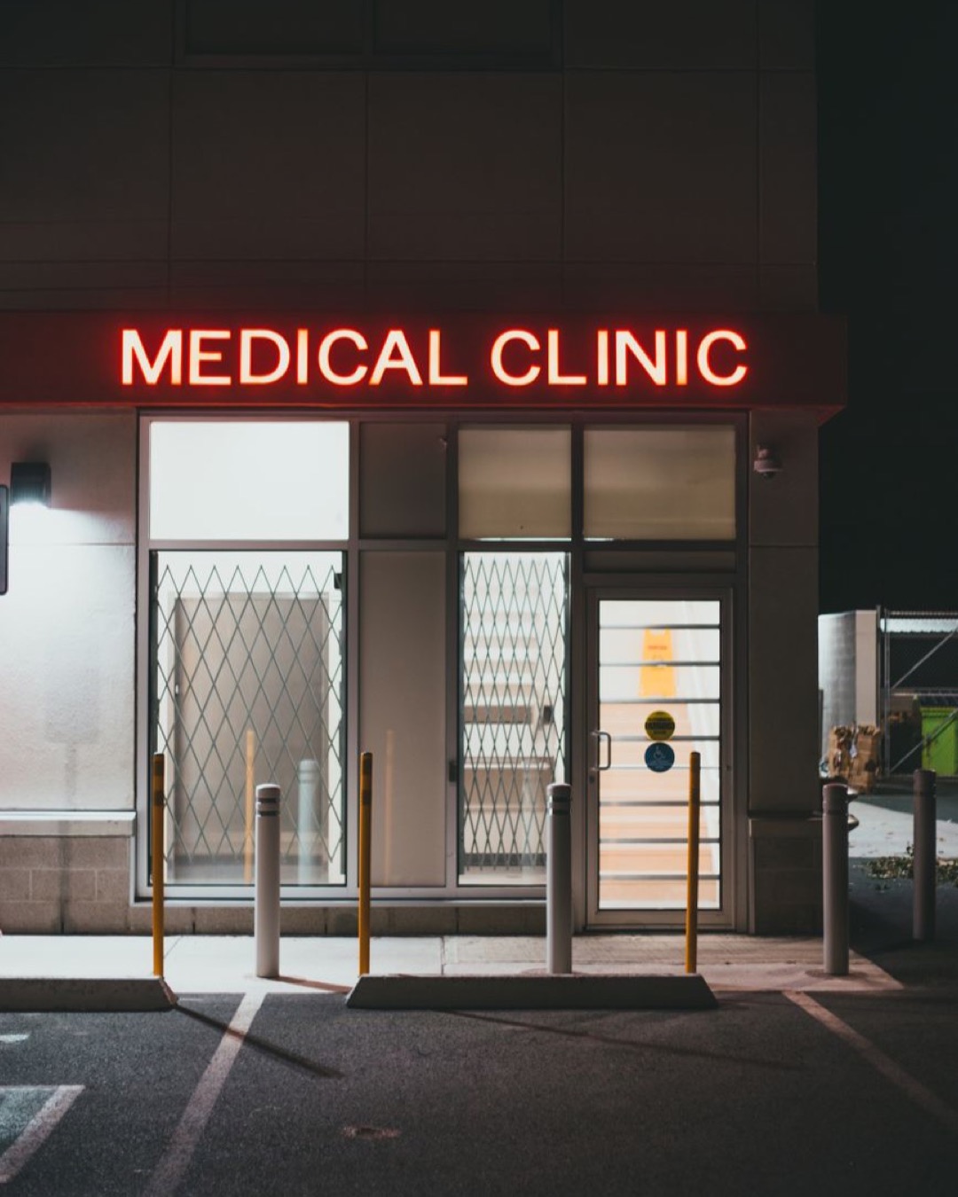 Night view of a medical clinic entrance illuminated by a neon sign in an empty parking area.