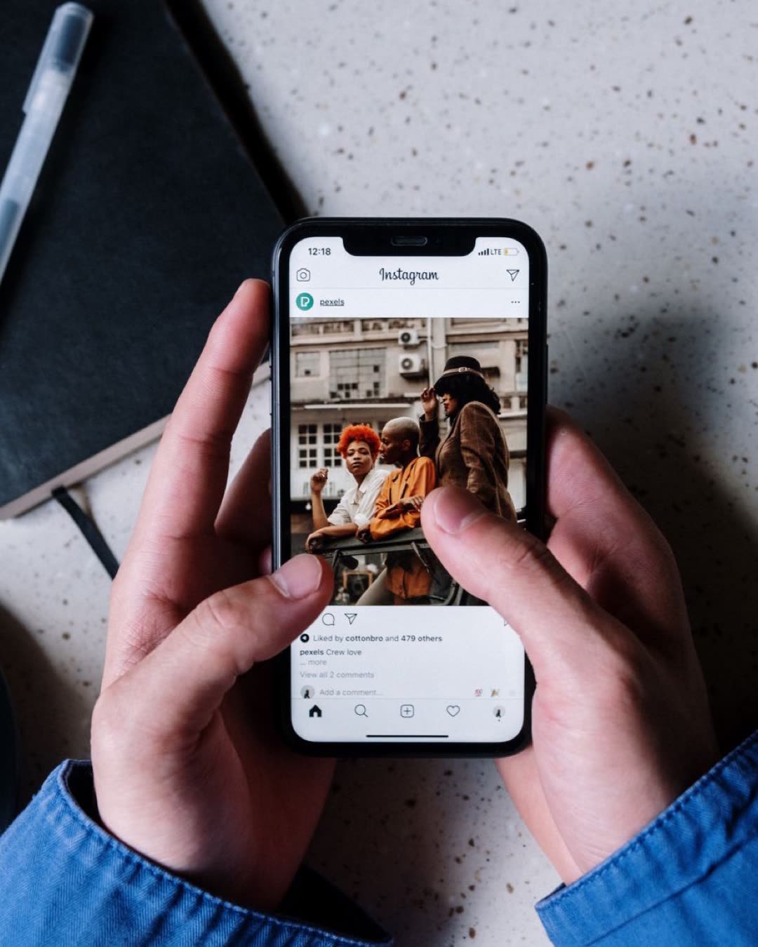 Close-up of hands holding a smartphone browsing Instagram with a notebook and pen nearby.