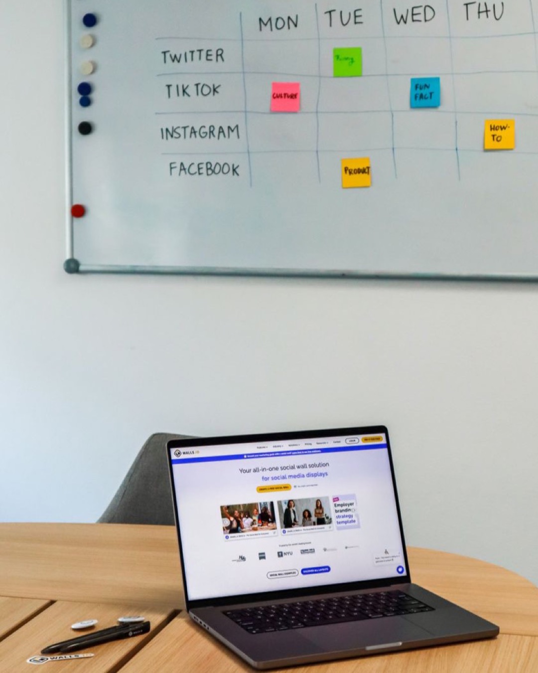 A modern office setup featuring a laptop and a whiteboard schedule for social media platforms.