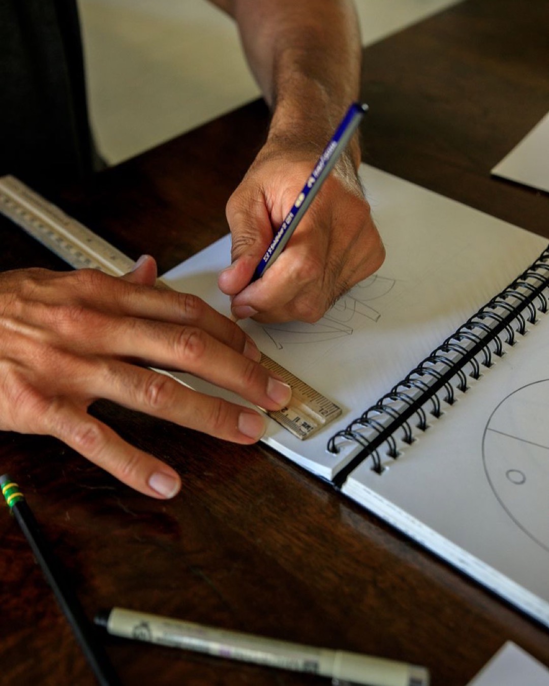 Hands of a man using a ruler and pencil for accurate line drawing in a notebook, showcasing precision and focus.
