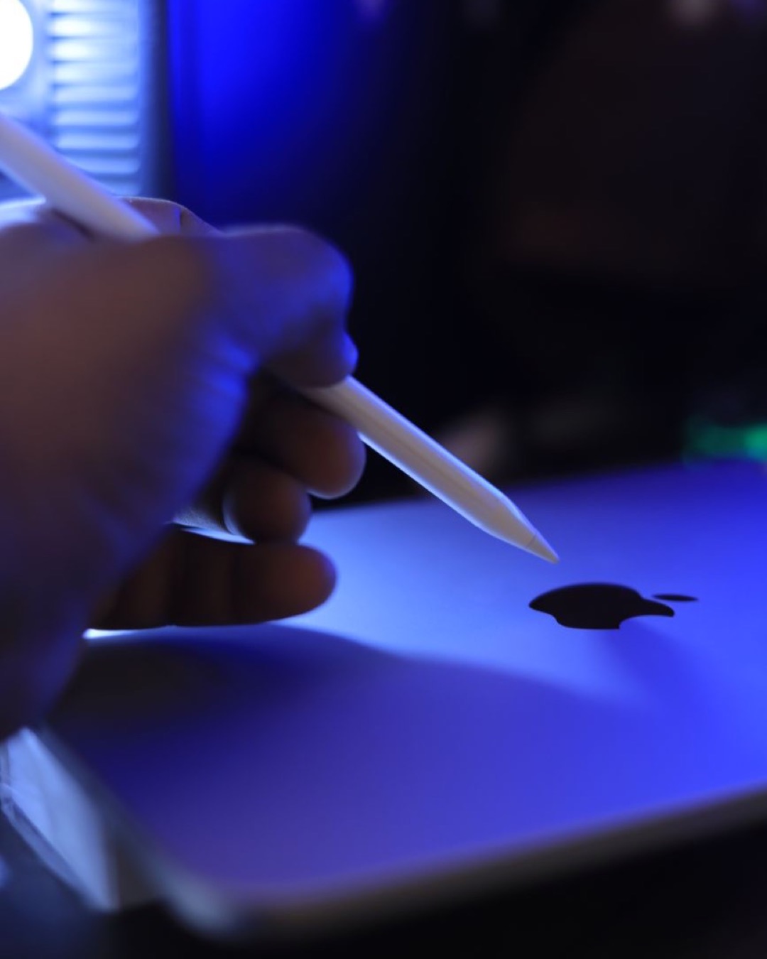 Close-up of a hand holding a stylus over an Apple device with a glowing apple logo.