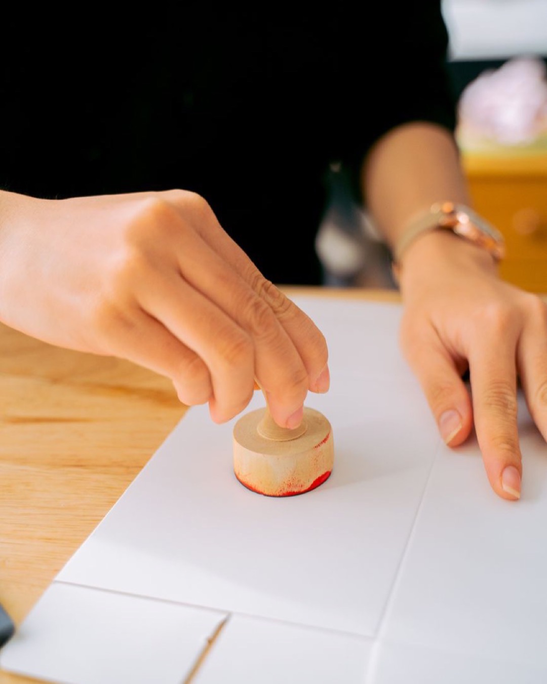 Close-up of a person using a wooden stamp on white paper indoors.