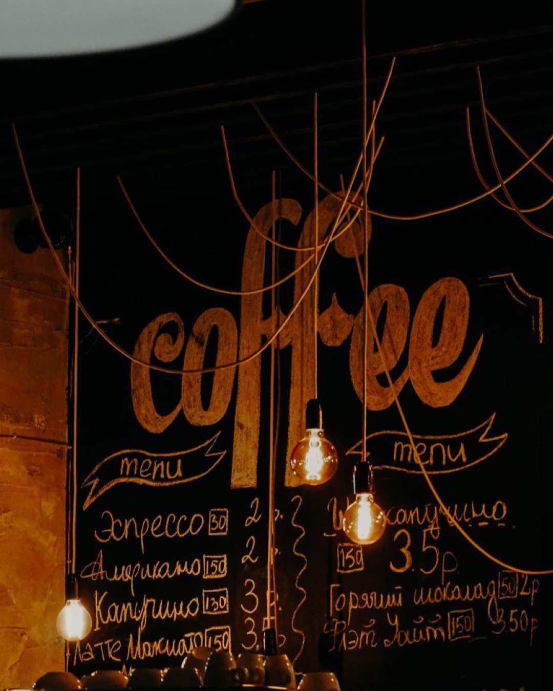Warm coffee shop ambiance featuring a chalkboard menu and stylish light bulbs.