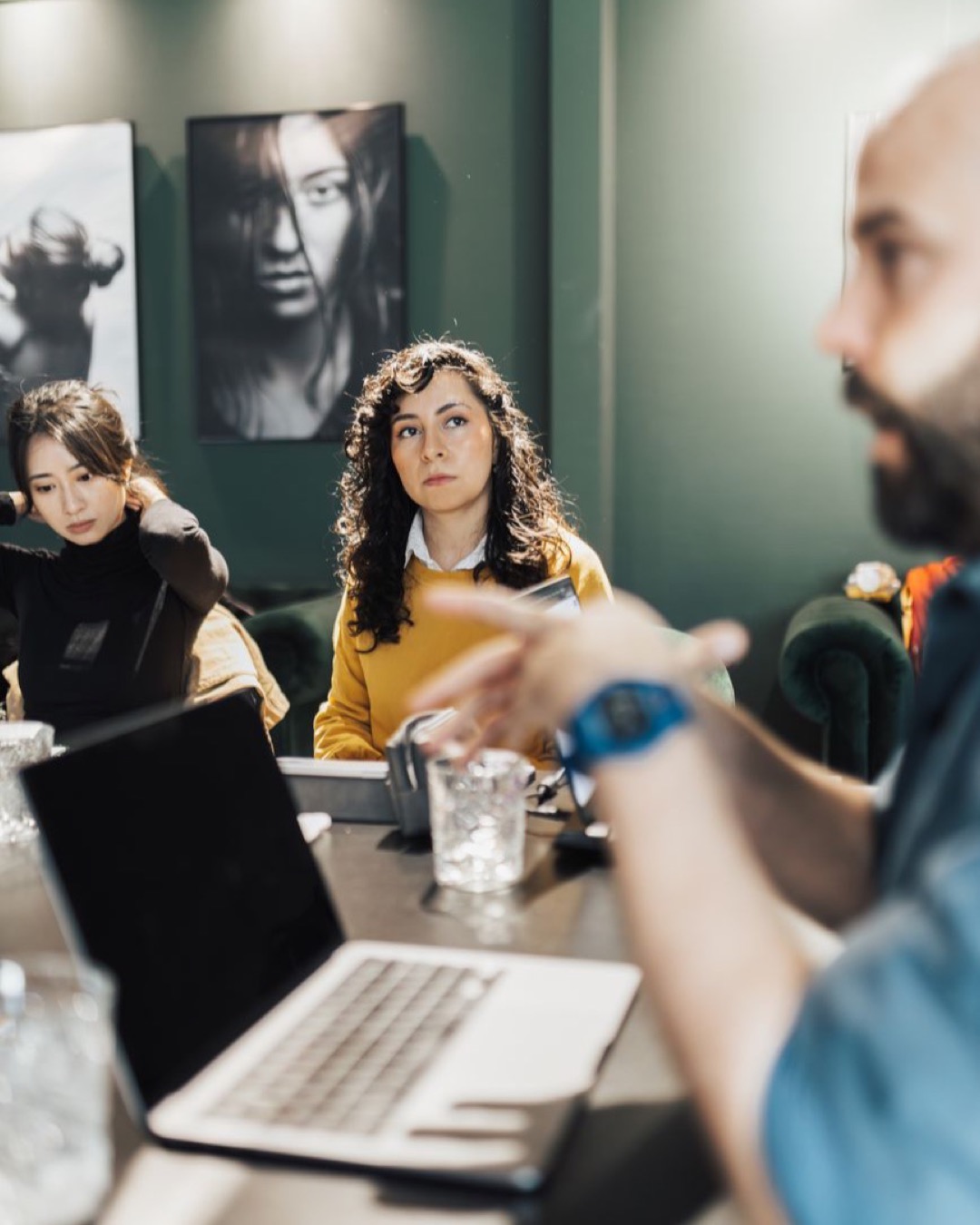 Professionals discussing projects around a conference table with laptops and notepads in an office.