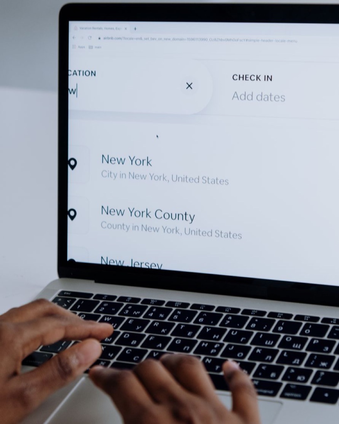 Hands typing on a laptop near New York location search screen.