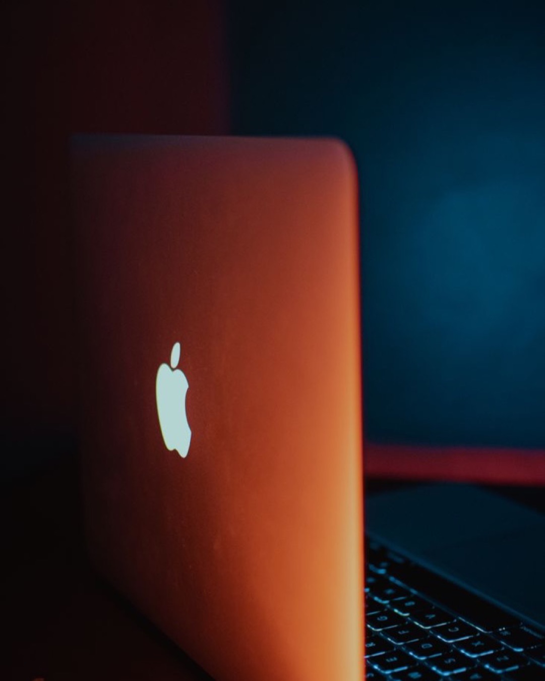 Minimalist laptop design featuring glowing Apple logo with dramatic lighting.