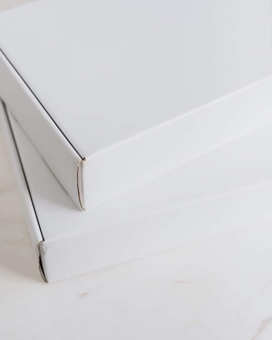 Simple white cardboard boxes stacked on a light marble surface, ideal for packaging mockups.