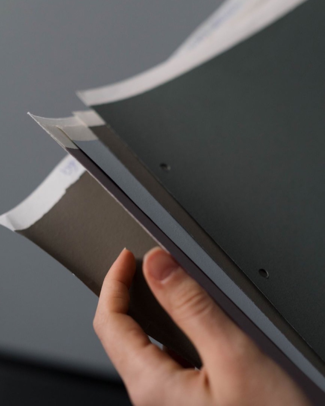 A close-up view of a hand holding paper samples, showcasing different textures and colors.