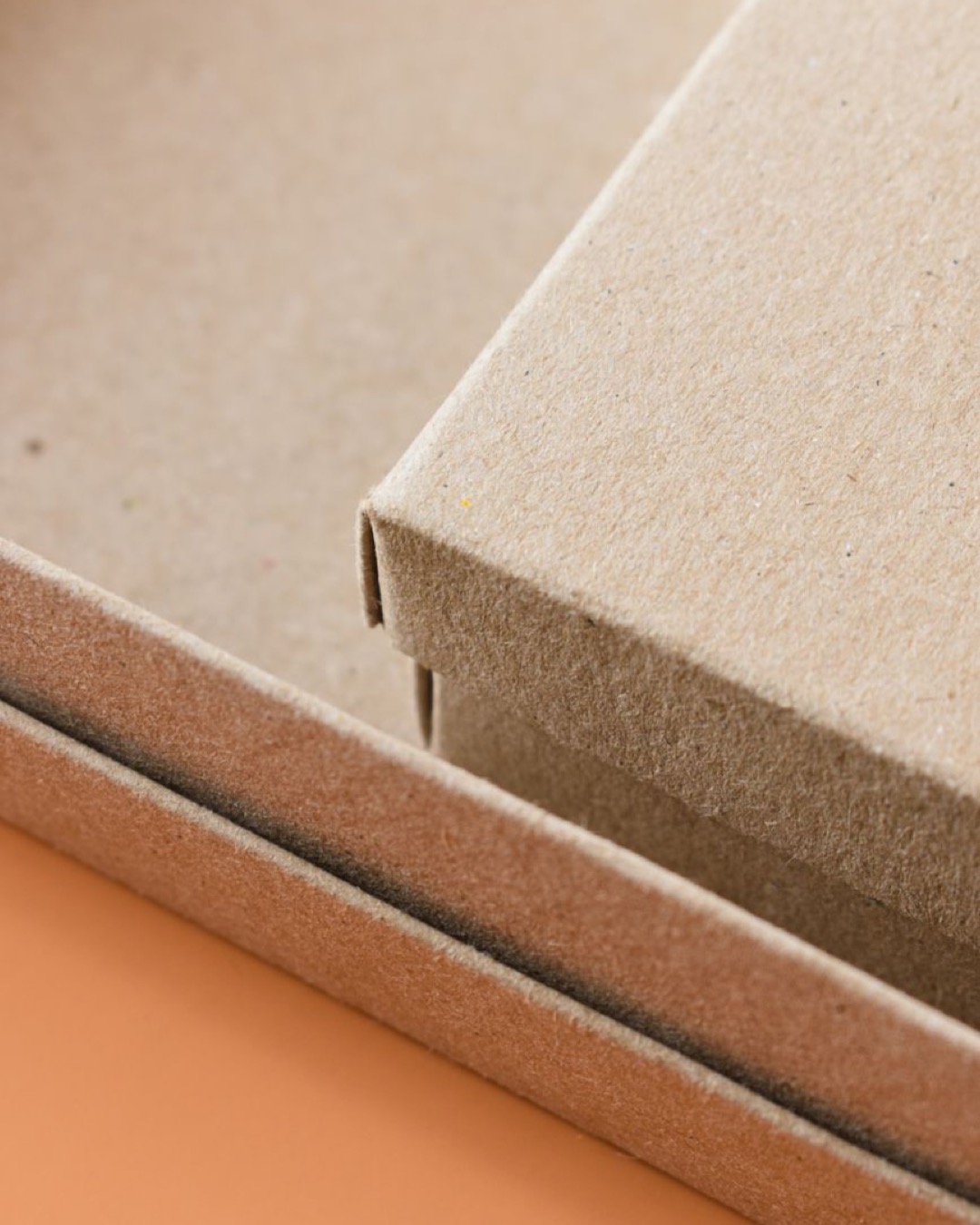 Minimalist close-up of eco-friendly cardboard packaging boxes on an orange background.