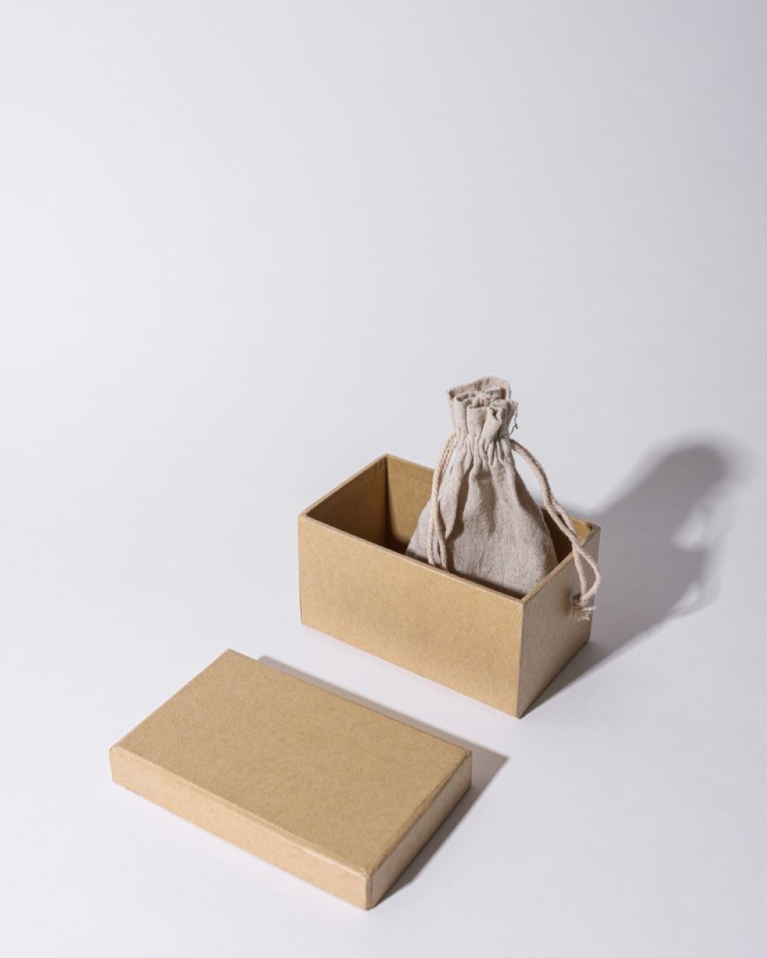 A minimalist kraft cardboard box with a linen pouch inside, under neutral lighting.