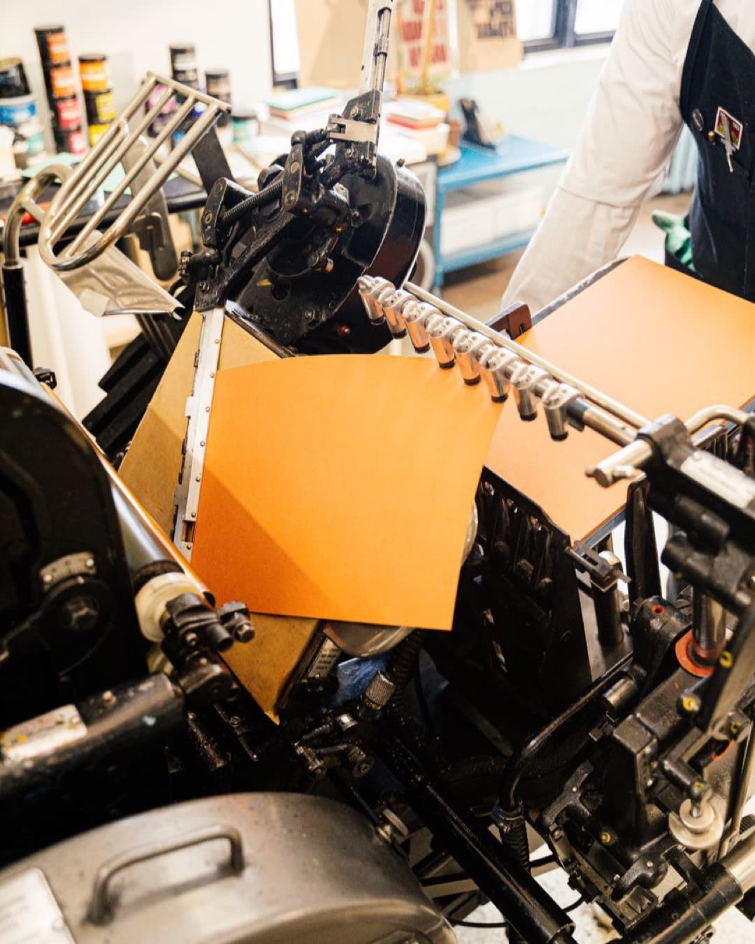 Close-up of a vintage printing press with orange paper, highlighting industrial craftsmanship.