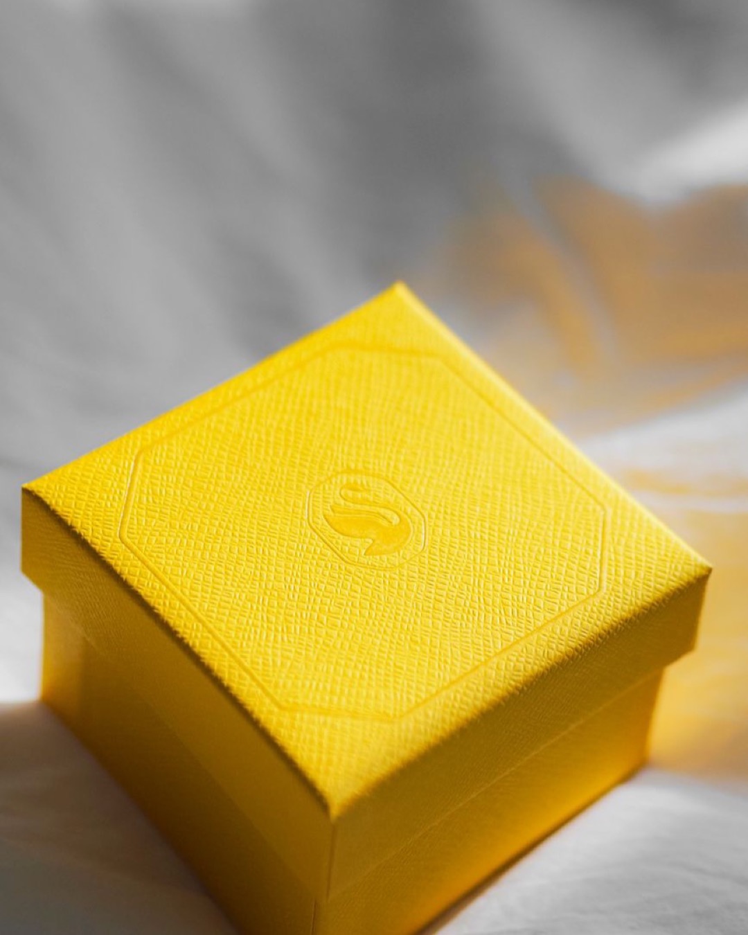 A vibrant yellow gift box with an embossed design on a textured surface, bathed in soft light.