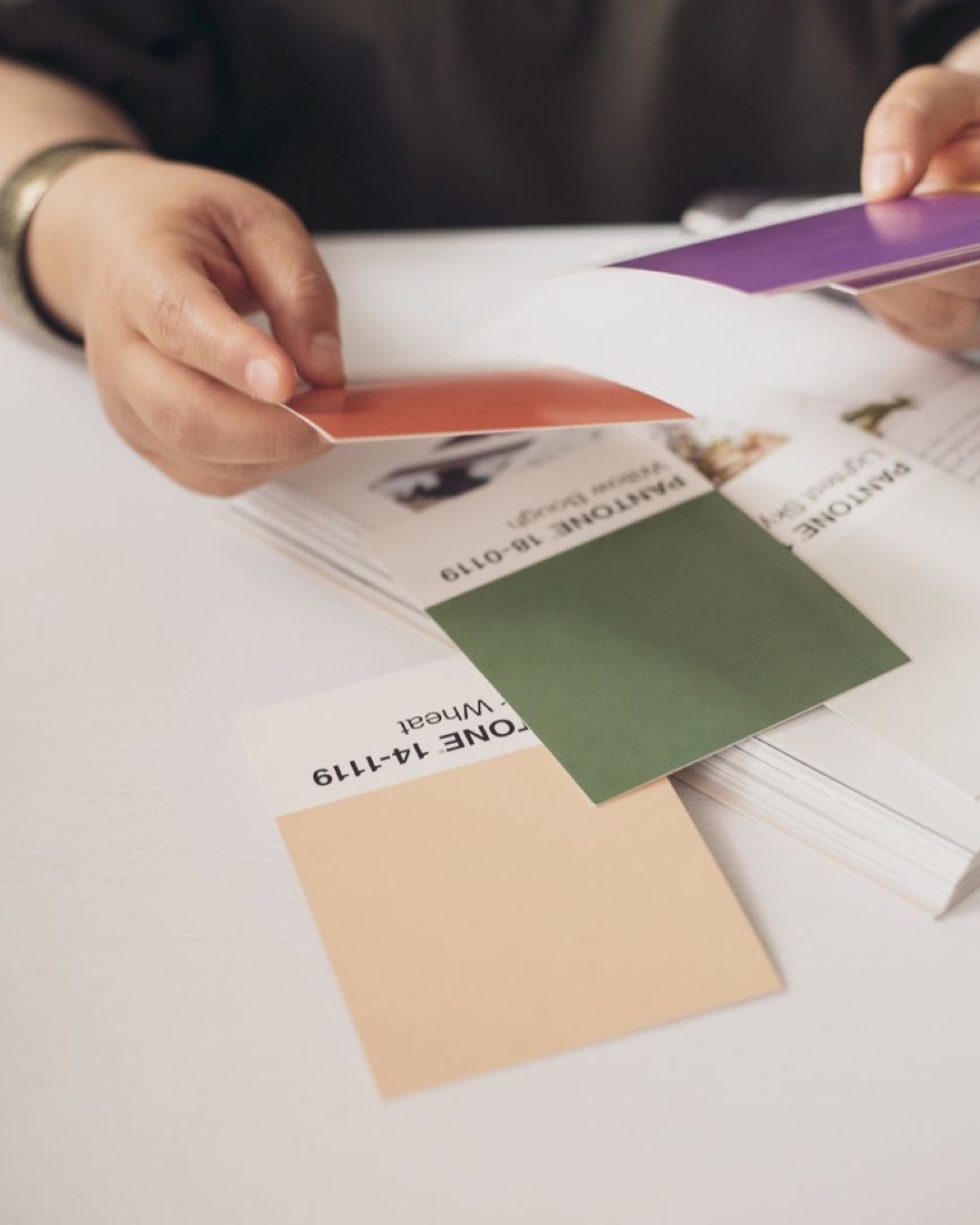 Close-up of hands selecting Pantone color swatches in a creative setting.