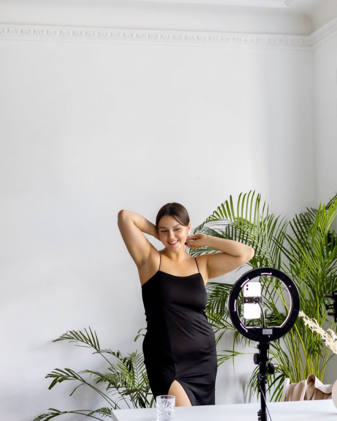 Young woman posing joyfully indoors with a camera setup, embodying modern lifestyle.