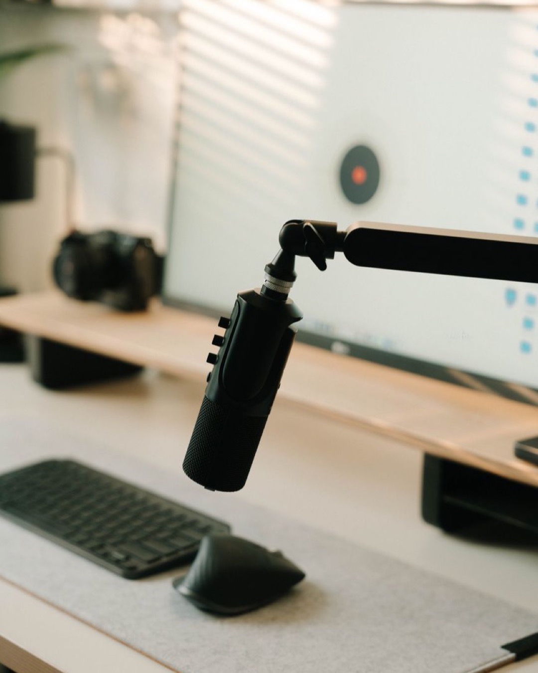 A sleek podcasting setup featuring a microphone, keyboard, and computer screen.